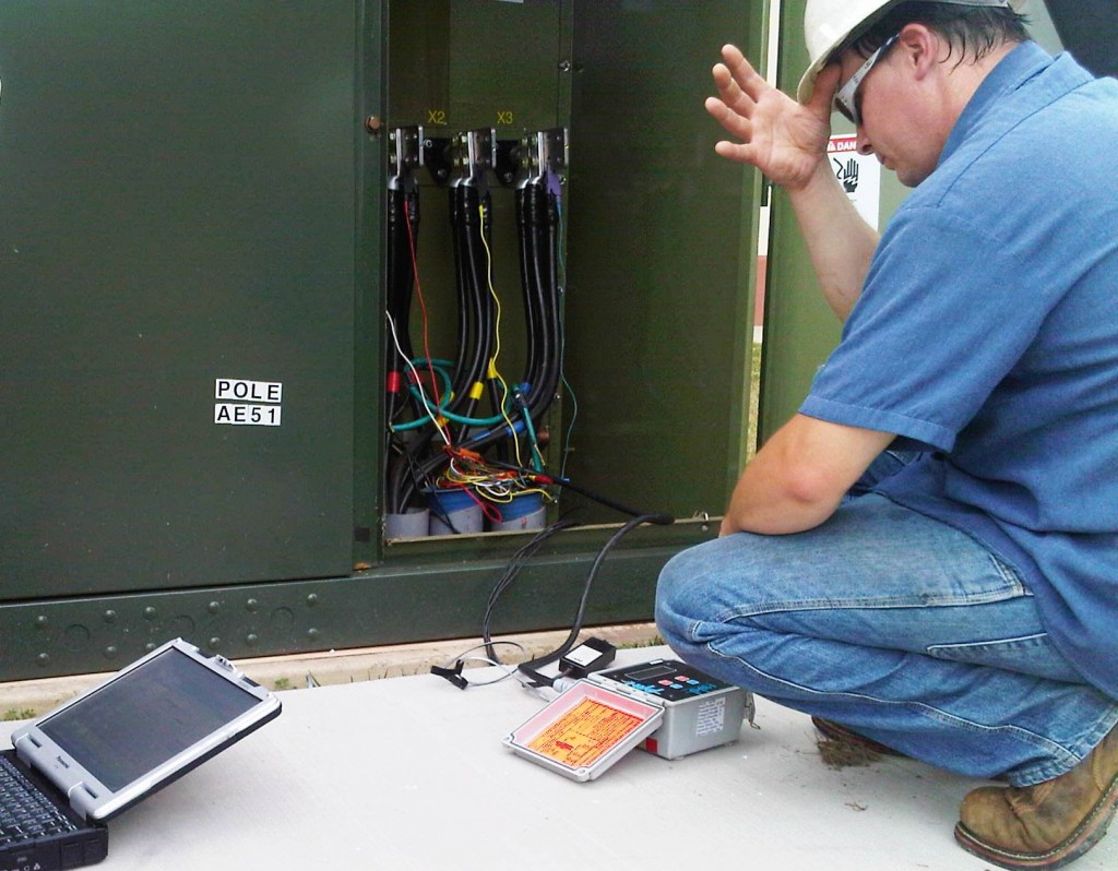 Technician testing an electrical cabinet with a laptop and meter